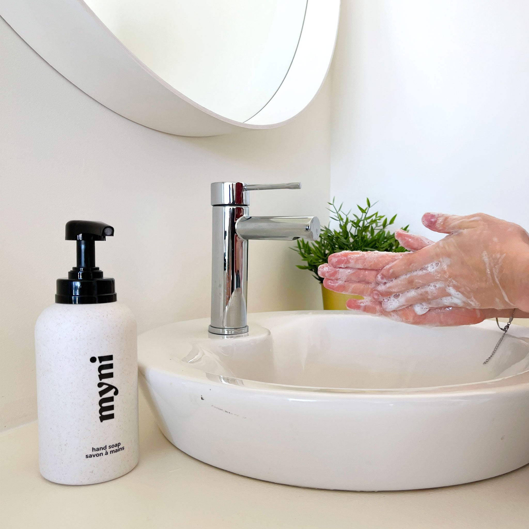 
                  
                    Person washing hands with soap next to a sink and 'myni' bottle.
                  
                